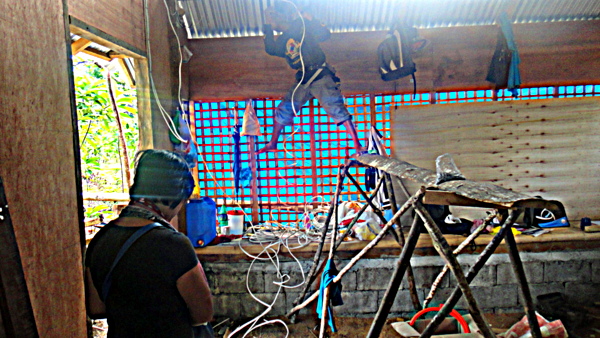 Joery balancing on the scaffold, installing wiring in the nipa hut